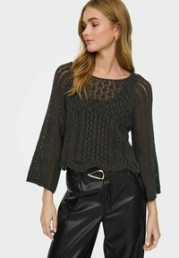 Pull en crochet noir avec une coupe ample, manches larges et un motif en tricot ouvert complexe, associé à un pantalon en cuir noir taille haute.