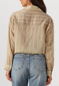 Lichtbeige shirt met witte verticale strepen, gemaakt van een zacht textiel met lange mouwen. Gekleed met blauwe spijkerbroek.
