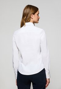 Camicia bianca a maniche lunghe con vestibilità sartoriale, orlo curvo e colletto standard. Presenta bottoni tono oro ai polsini.