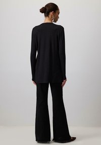 Čierny top s dlhými rukávmi a voľným strihom, s okrúhlym výstrihom. V kombinácii s čiernymi rozšírenými nohavicami, ktoré predstavuju elegantný, minimalistický dizajn.