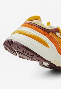Zapatillas deportivas con una parte superior en naranja y amarillo, acentos en marrón, paneles de malla y una suela blanca con una unidad de amortiguación visible.