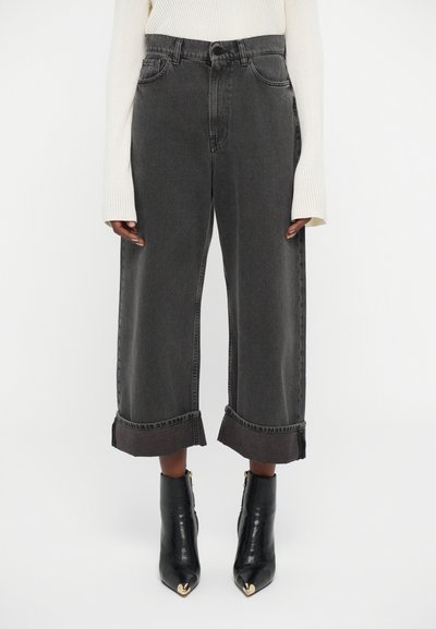 Person wearing high-waisted, wide-leg black cropped jeans with large cuffs, a white long-sleeve sweater, and black pointed toe ankle boots.