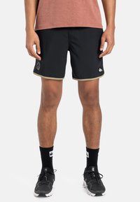 Sorte svømmebukser med guldkant, elastisk talje og logoaccent. Båret med sorte sokker og løbesko, hvilket fremhæver et sporty look.