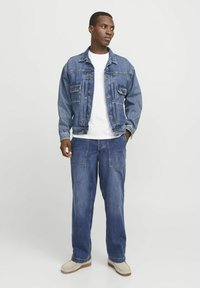 Chaqueta de mezclilla con dos bolsillos frontales, llevada sobre una camiseta blanca; combinada con pantalones de mezclilla holgados de cintura alta. Detalles ligeramente desgastados.