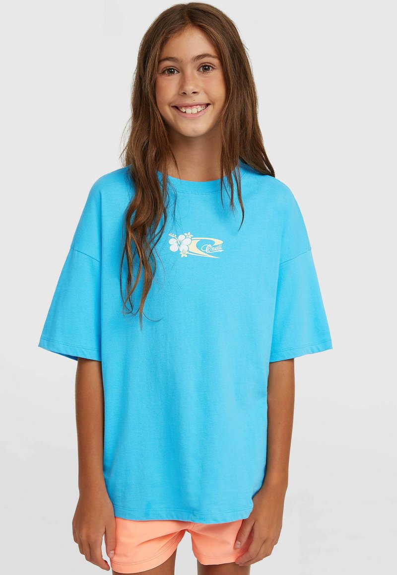 Blaues Baumwoll-T-Shirt mit kurzen Ärmeln und lockerem Schnitt, mit einem kleinen weißen Blumenlogo auf der Brust. Kombiniert mit korallenroten Shorts.