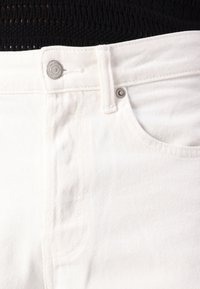 White denim jeans featuring a classic five-pocket design, button closure, and subtle diagonal ribbed texture.