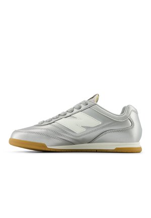 Silver athletic shoe with a smooth, shiny surface, white logo on the side, textured gray laces, and a gum rubber sole.