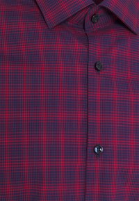 Chemise à carreaux rouge et bleu marine avec des boutons noirs, montrant les détails du col et de la patte de boutonnage.