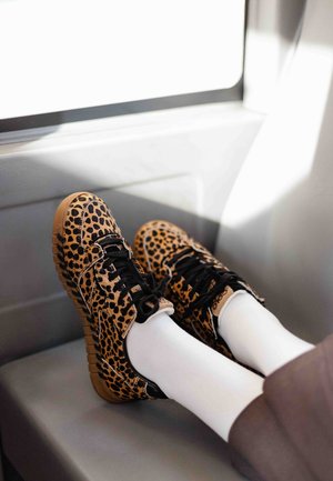 Leopardmønstret sneakers med sorte detaljer, tekstureret overflade og gummisåler i naturlig farve. Bruges med hvide sokker på et sæde.