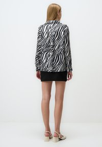 Camicia a righe zebra in bianco e nero con maniche lunghe, colletto e bottoni, abbinata a una mini gonna nera e sandali con tacco a blocco color crema.