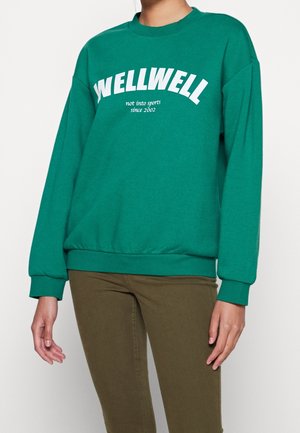 Zelená mikina s bílým textem "WELLWELL" a "ne sportuji od roku 2002." Volný střih s žebrovanými manžetami a lemem.