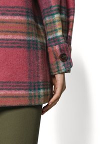 Pink and green plaid wool jacket with a buttoned cuff, featuring a soft texture and dropped shoulder design.