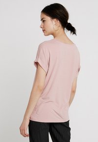 Rosa t-skjorte i bomull med rullet kort erm, rund hals og glatt tekstur, sett fra baksiden mot en ensfarget bakgrunn.