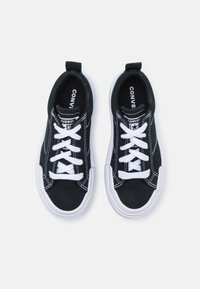 Melna auduma apavi ar baltiem šņorēm, gumijas zole un kontrastējoši šuvuma detaļas. Zīmola etiķete redzama katrā apavā iekšā.