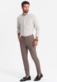 Licht gestreepte, lange mouwen shirt in beige en wit, gecombineerd met nauwsluitende bruine broek en zwarte instappers, met een moderne pasvorm.
