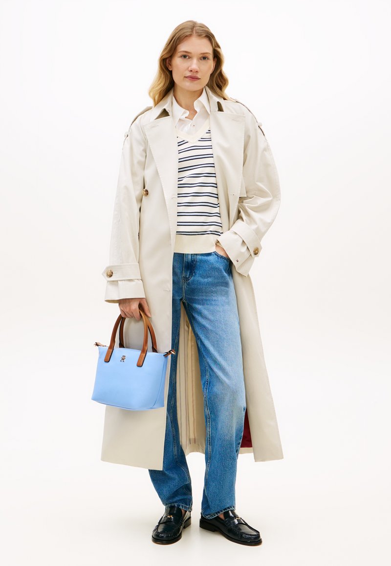 Μπεζ καμπαρντίνα με επωμίδες στους ώμους, λευκό ριγέ τοπ, μπλ ε τσάντα με καφέ λαβές, μπλε τζιν και μαύρα παπούτσια. Απλός σχεδιασμός.