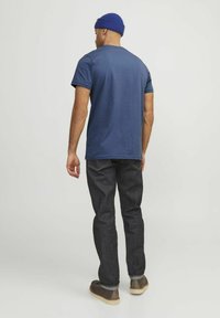 Tricou din bumbac bleumarin cu mâneci scurte, asociat cu blugi negri. Outfitul este completat cu pantofi maro și o căciulă croșetată albastră.