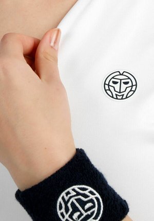 Mano ajustando tela blanca con logo estilizado de rostro en blanco y negro; la muñeca lleva una pulsera negra con un diseño abstracto blanco.