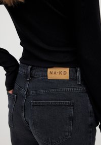 Juodi džinsai turi odinį etiketę su išsiuvinėtu "NA-KD" užpakalyje. Medžiaga turi klasikinį, lygią tekstūrą ir prigludusią išvaizdą.