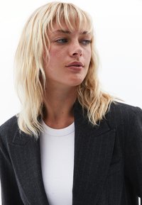 Kulgrå skræddersyet blazer med pynte-striber og notch-lapel, båret over en struktureret hvid ribbet skjorte, der har en glat stofoverflade.