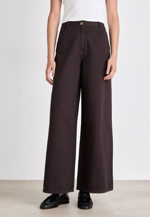 Pantaloni in cotone marroni a gamba larga con chiusura a bottone, tasche anteriori e taglio dritto, abbinati a scarpe nere su uno sfondo neutro.