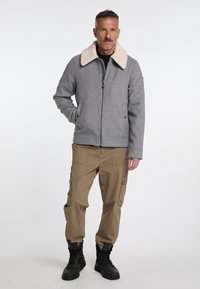 Grijze wollen jas met een crème schapenvacht kraag, ritsluiting en zijzakken; gecombineerd met beige cargo broeken en zwarte laarzen.