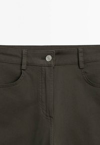 Gros plan sur la ceinture et les poches avant d’un pantalon marron foncé avec un bouton argenté et des passants de ceinture.