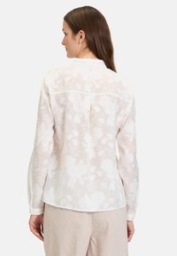 White embroidered blouse featuring floral patterns, long sleeves, and a buttoned collar. Lightweight and semi-sheer fabric with a relaxed fit.