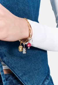 Goldkettchen-Armband mit Anhängern: ein goldenes rechteckiges Schild, eine silberne Eule, ein roter Email-Pilz und die Zahl "21" in Silber mit Strasssteinen.