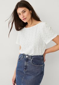 Hvid øjenlåg bluse med korte ærmer og rund halsudskæring, parret med en høj talje denimnederdel. Glat tekstur og åndbart design.