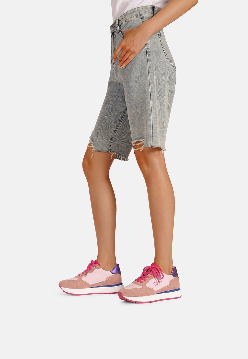 Shorts in denim chiaro con effetto usurato e orli sfrangiati, abbinati a sneakers sportive rosa e viola con pannelli in suede morbido.