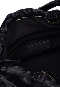 Interno di una borsa nera in pelle con cordoncino, caratterizzato da una trama liscia, tasca con zip e dettagli in metallo dorato con etichetta del marchio.