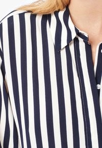 Camicia con bottoni caratterizzata da strisce verticali blu navy e bianche, colletto a punta e tessuto leggero e liscio con una sottile texture.