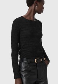 Zwarte, gestructureerde blouse met lange mouwen en een getailleerde pasvorm, gecombineerd met hoge zwarte leren broek en een riem met gouden accenten.