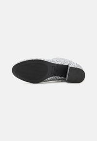 Glittering silver slip-on shoe with a textured upper, featuring a rubber outsole with a wavy tread pattern for grip.