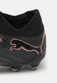 Scarpa da calcio nera con tomaia in mesh testurizzato, logo Puma rosa, dettagli lisci e tacchetti trasparenti per la trazione.