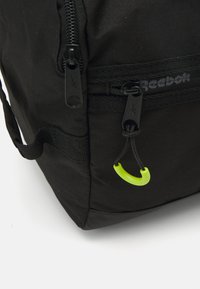 Black fabric backpack featuring a prominent zipper, a green accent on the zipper pull, and textured material.