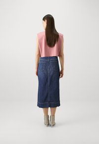 Rosa kort topp med brede skuldre, kombinert med et langt, mørkeblått denimskjørt med baklommer og en søm detaljer ved kanten.
