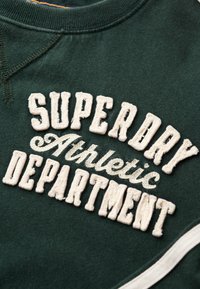 Mørkegrøn sweatshirt med hvid broderet tekst der står "SUPERDRY Athletic DEPARTMENT" med glat stof og rund hals.