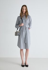 Stripet skjortekjole i lys og mørk blå, knapp-up design, belte i midjen, lange ermer, kombinert med en mønstret crossover bag og svarte hæler.