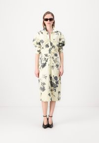 Floral print dress in pale yellow with gray patterns; button-down front, gathered sleeves, knee-length cut, paired with black open-toe heels.