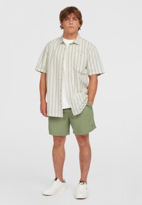 Short-sleeve, green-striped button-up shirt with a pocket, paired with olive green shorts. White sneakers complete the look.