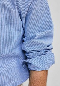 Camicia a righe blu e bianche con maniche arrotolate, realizzata in tessuto leggero, caratterizzata da una texture liscia e un motivo delicato.