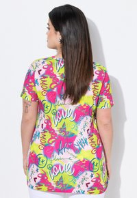 T-shirt graphique à manches courtes en rose et vert, présentant un texte coloré, des cœurs et des motifs de papillons sur un tissu doux et lisse.