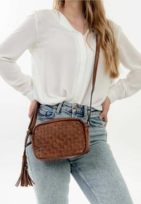 Borsa a tracolla in pelle marrone con motivo floreale in rilievo e dettaglio con nappina, dotata di chiusura con zip e tracolla regolabile.
