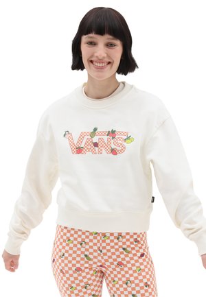 Suéter blanco con el diseño de cuadros naranjas de "VANS", adornado con gráficos de frutas. Combinado con pantalones de cuadros melocotón y blancos.