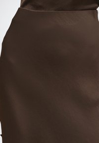 Gros plan d'une jupe en cuir lisse brun foncé avec une texture subtile et des plis naturels.