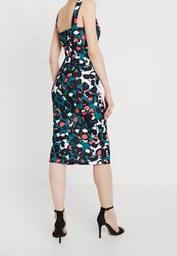 Robe cintrée avec un motif floral audacieux en bleu sarcelle, rose et noir, présentant un dos carré, des bretelles larges et un ourlet à hauteur du genou. Escarpins noirs.