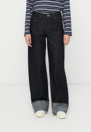 Dark blue wide-leg jeans with a high waist, featuring rolled cuffs and contrasting hem. Paired with white sneakers and a striped top.