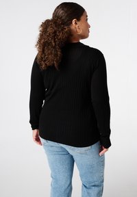 Zwarte geribbelde top met lange mouwen en een ronde hals, gecombineerd met lichtblauwe high-waisted spijkerbroek. De stof lijkt zacht en gestructureerd.